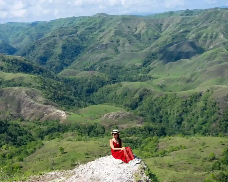 A traveller sitting on a rock above a green valley in the Tanarara hills, East Sumba