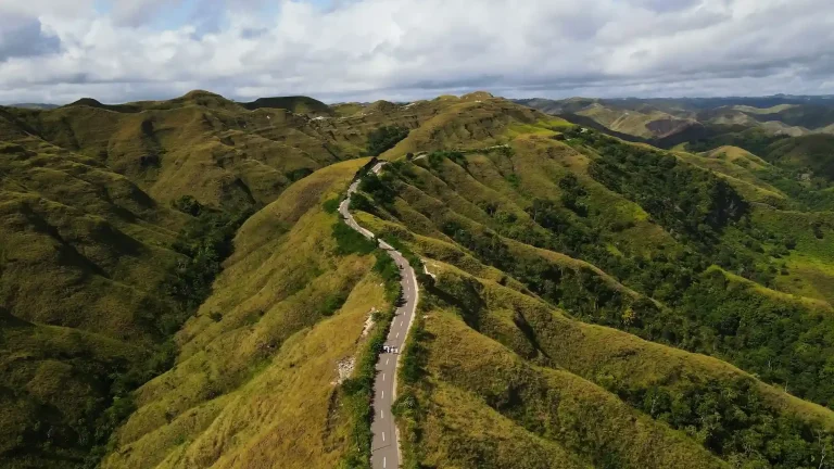 Aerial view of a road winding along the green ridges of the Tanarara hills in East Sumba