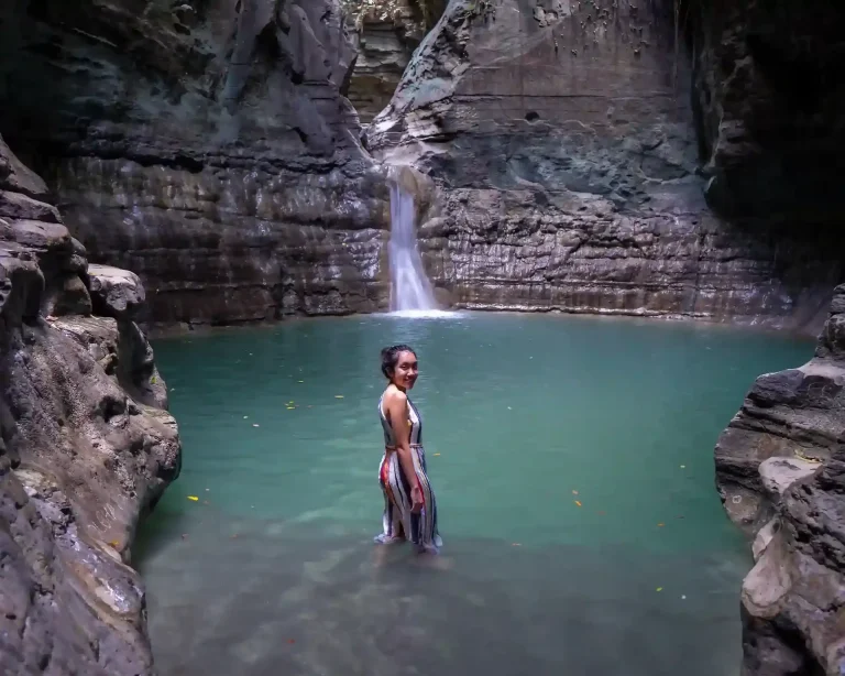 A lone traveller wading in the emerald pool beneath the canyon walls of Waimarang Waterfall, East Sumba